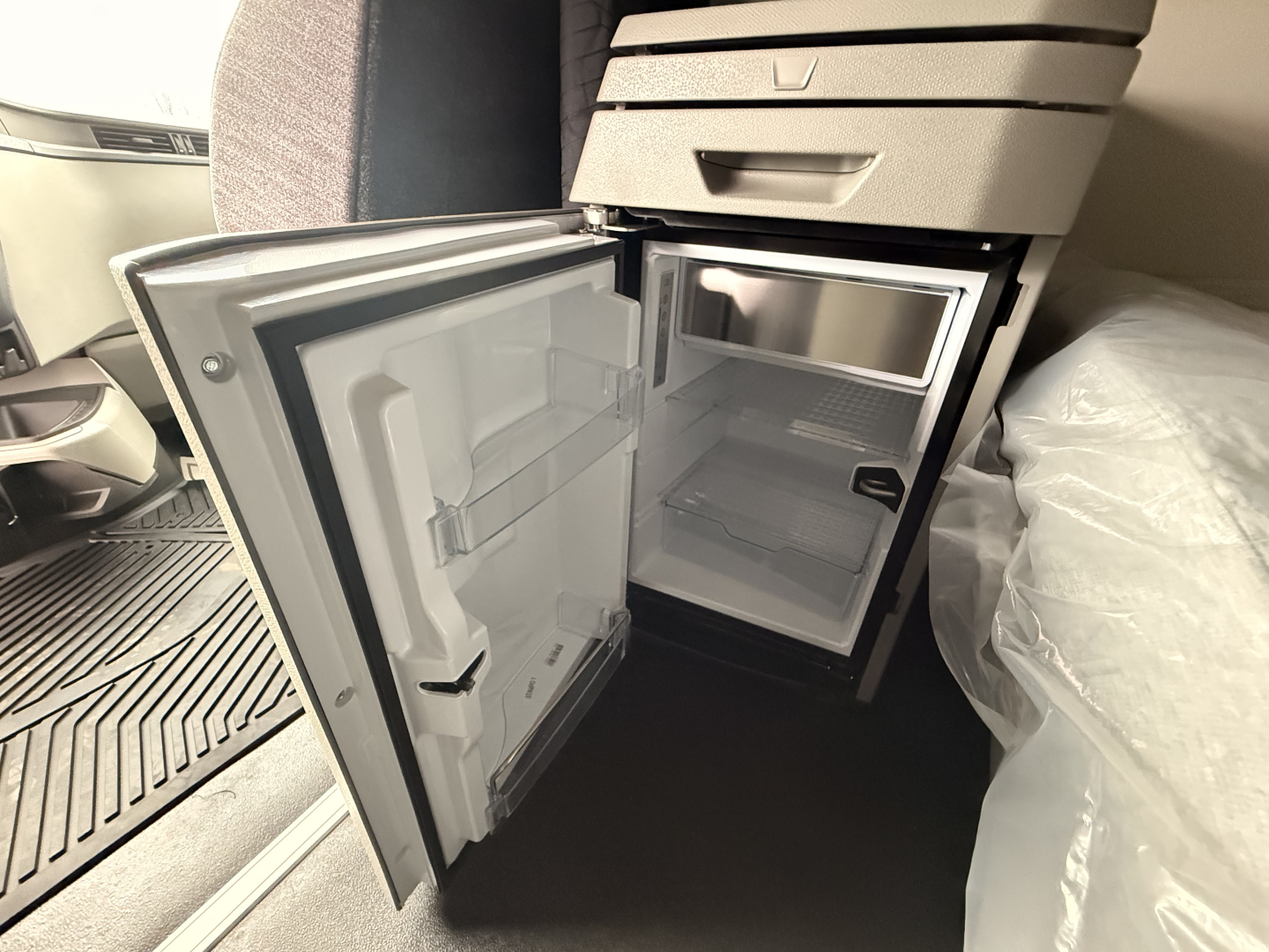 Volvo VNL64T860 cab interior showing open kitchenette fridge/freezer area with small appliance shelf and storage compartments.