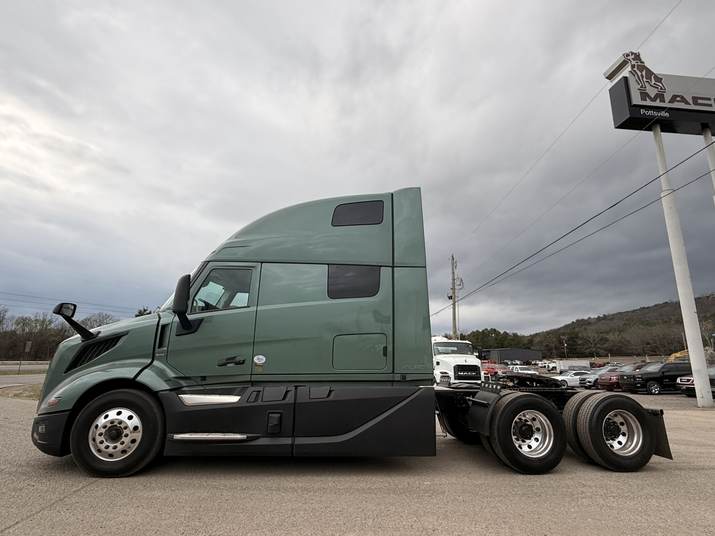 Truck side view showing 2027 Volvo VNL64T860 conventional sleeper with green cab, dual rear axles, and side mirrors.