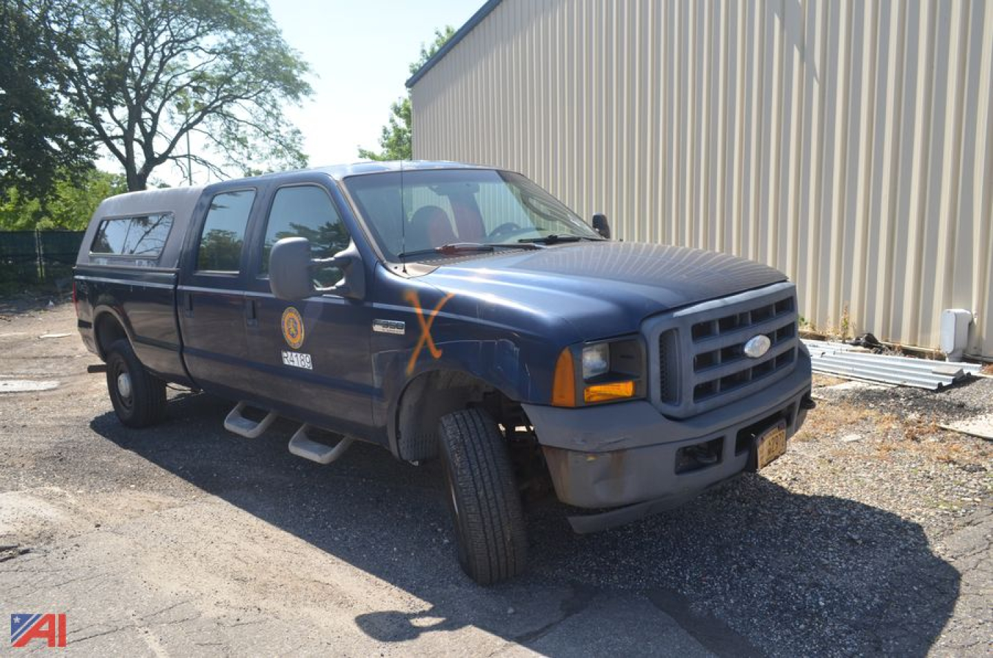 Ford F-350 Super Duty pickup truck with crew cab and utility cap, blue exterior, front-right view, orange X marks on fender, badge logos visible.