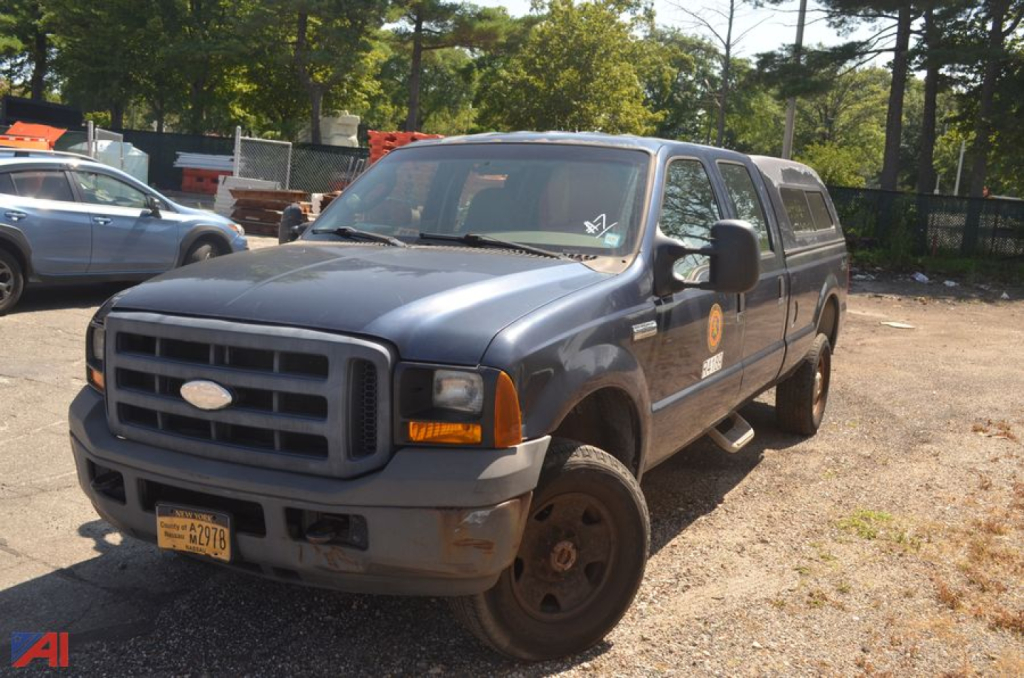 Ford F-350 Super Duty pickup truck in a used lot showing front grille and passenger side with utility van in background.