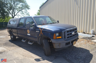 Ford F-350 Super Duty pickup truck with crew cab and utility cap, blue exterior, front-right view, orange X marks on fender, badge logos visible.