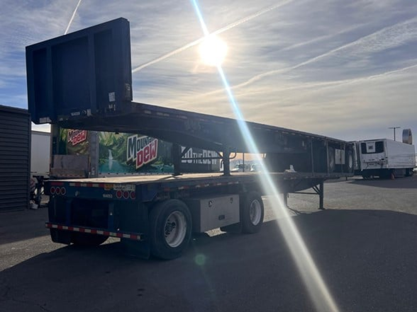 Flatbed trailer by Great Dane with a large loading ramp raised at the rear, parked in a lot with other trailers visible.