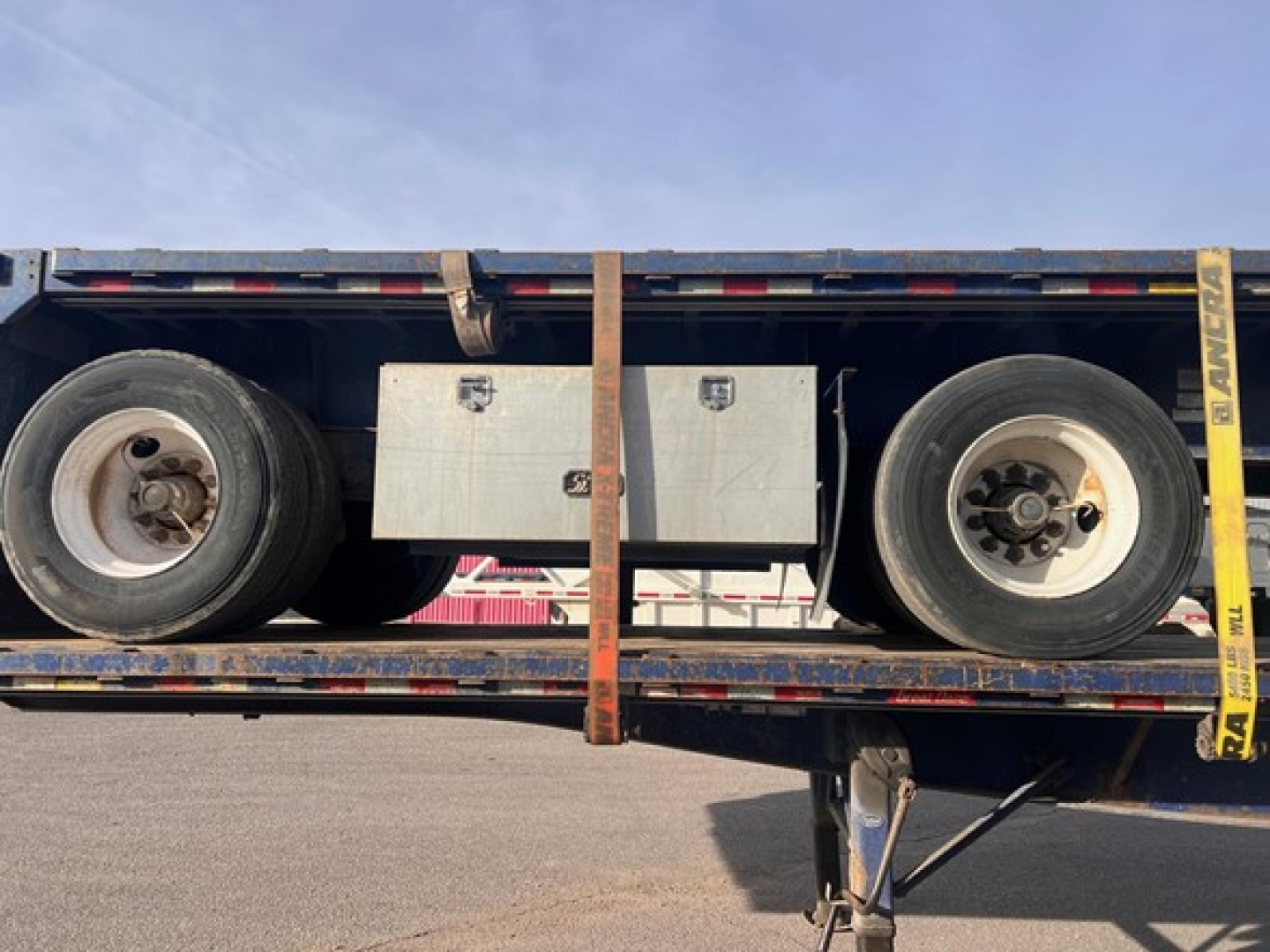 Flatbed trailer image showing wheels and a metallic toolbox centered on the frame.