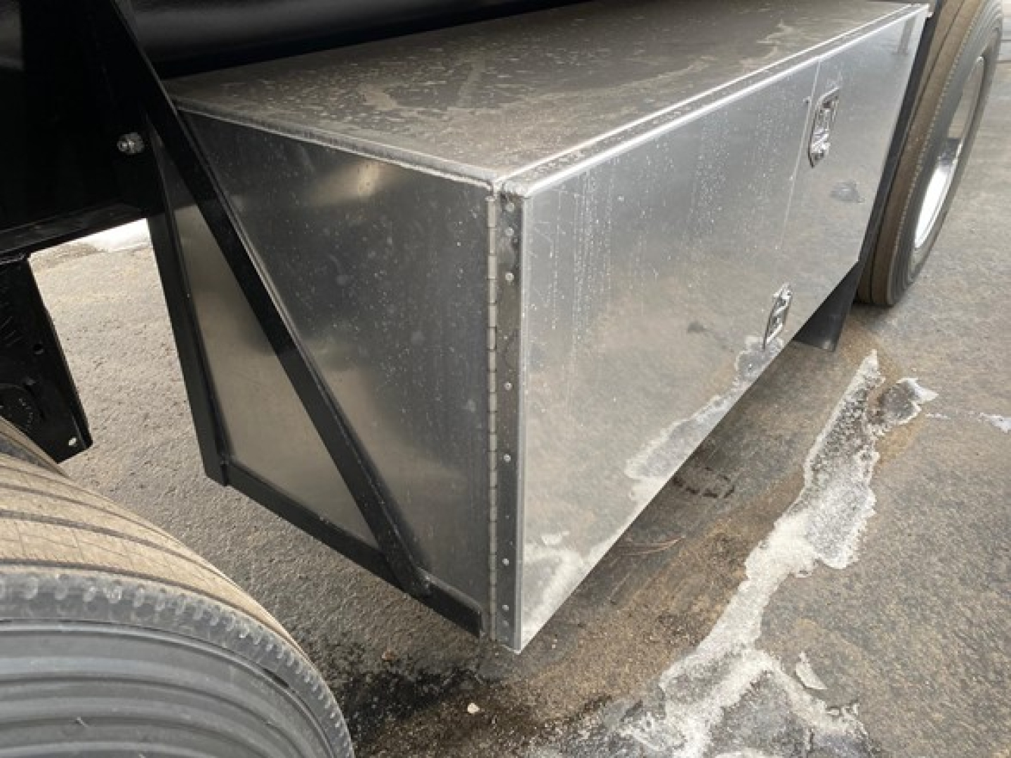 Flatbed trailer tool box mounted under trailer showing aluminum diamond-plate toolbox with riveted seams and handles.