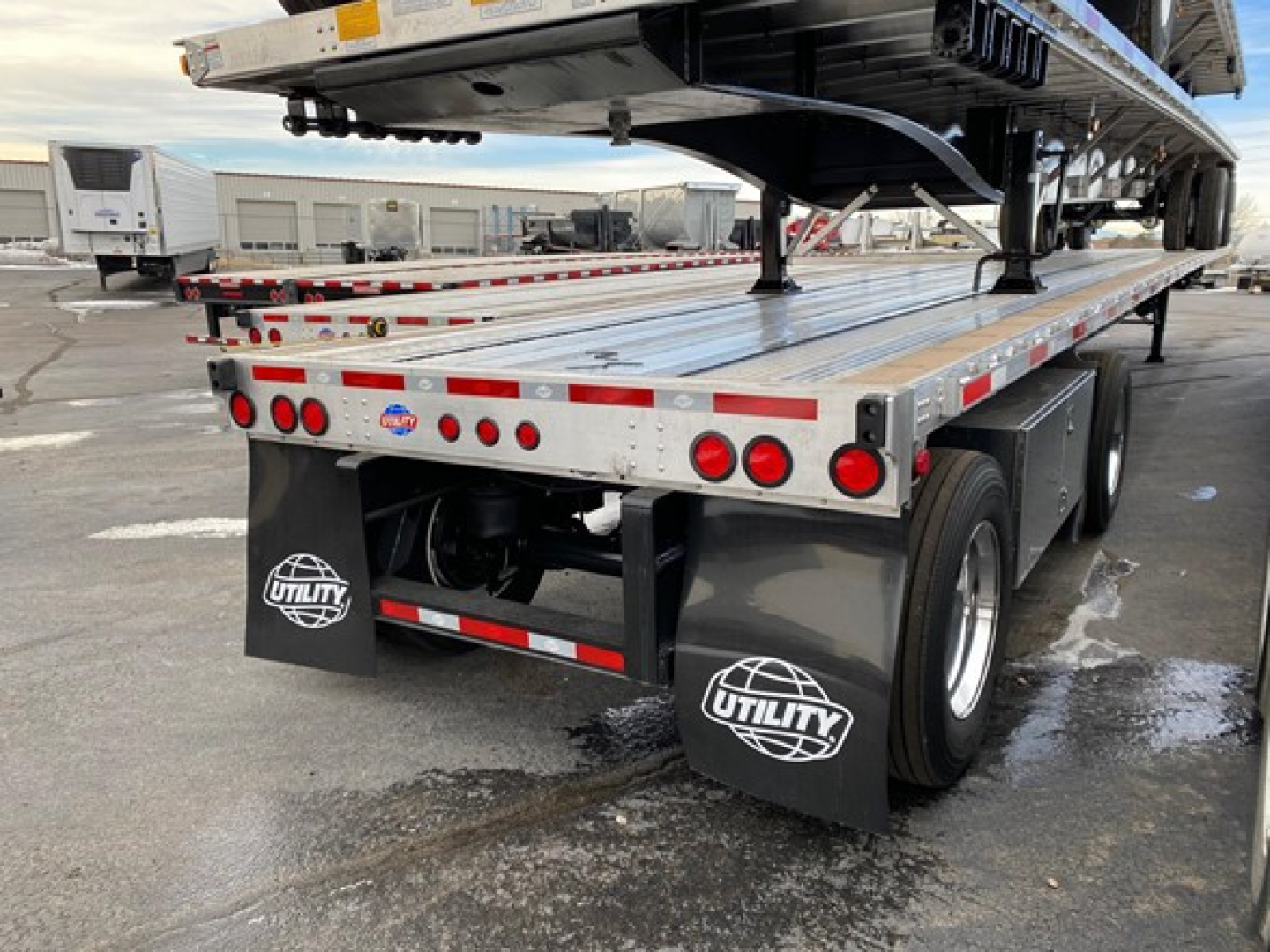 Flatbed trailer showing Utility brand mud flaps and rear lights with a raised upper deck and trailer wheels.