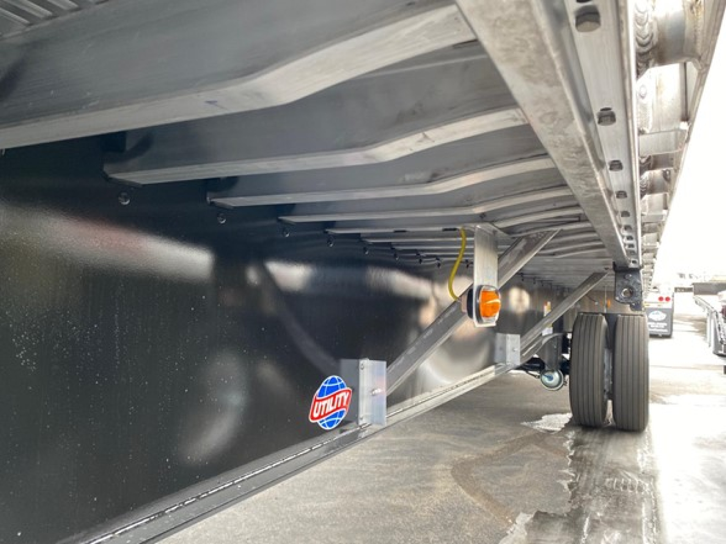 Flatbed trailer underside view showing black metal frame, side marker light, support beams, and wheel area.