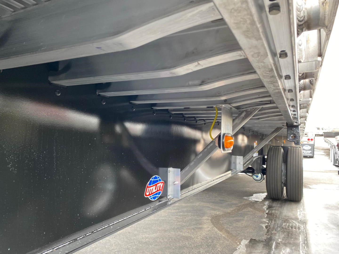 Underbelly of a new Utility 4000AE flatbed trailer showing frame, side rail, and spare hubs; reflective sticker visible along the black underside.