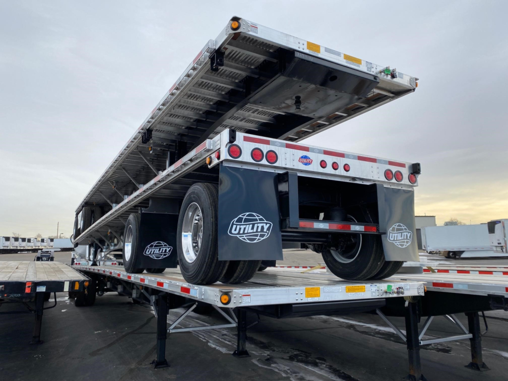Utility 4000AE flatbed trailer on a transport bed, rear view with hydraulic lift and dual tires visible, Utility logo mud flaps.