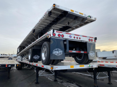 Utility 4000AE flatbed trailer on a transport bed, rear view with hydraulic lift and dual tires visible, Utility logo mud flaps.