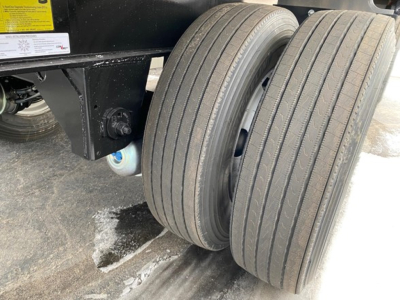 Trailer rear dual axles with four solid tires and black chassis showing wheel wells and mounting hardware.