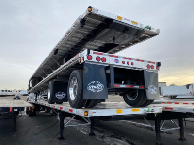 Utility flatbed trailer with a raised bed and rear wheels visible, showing Utility branding on mud flaps and undercarriage, platform details and reflective safety tape.