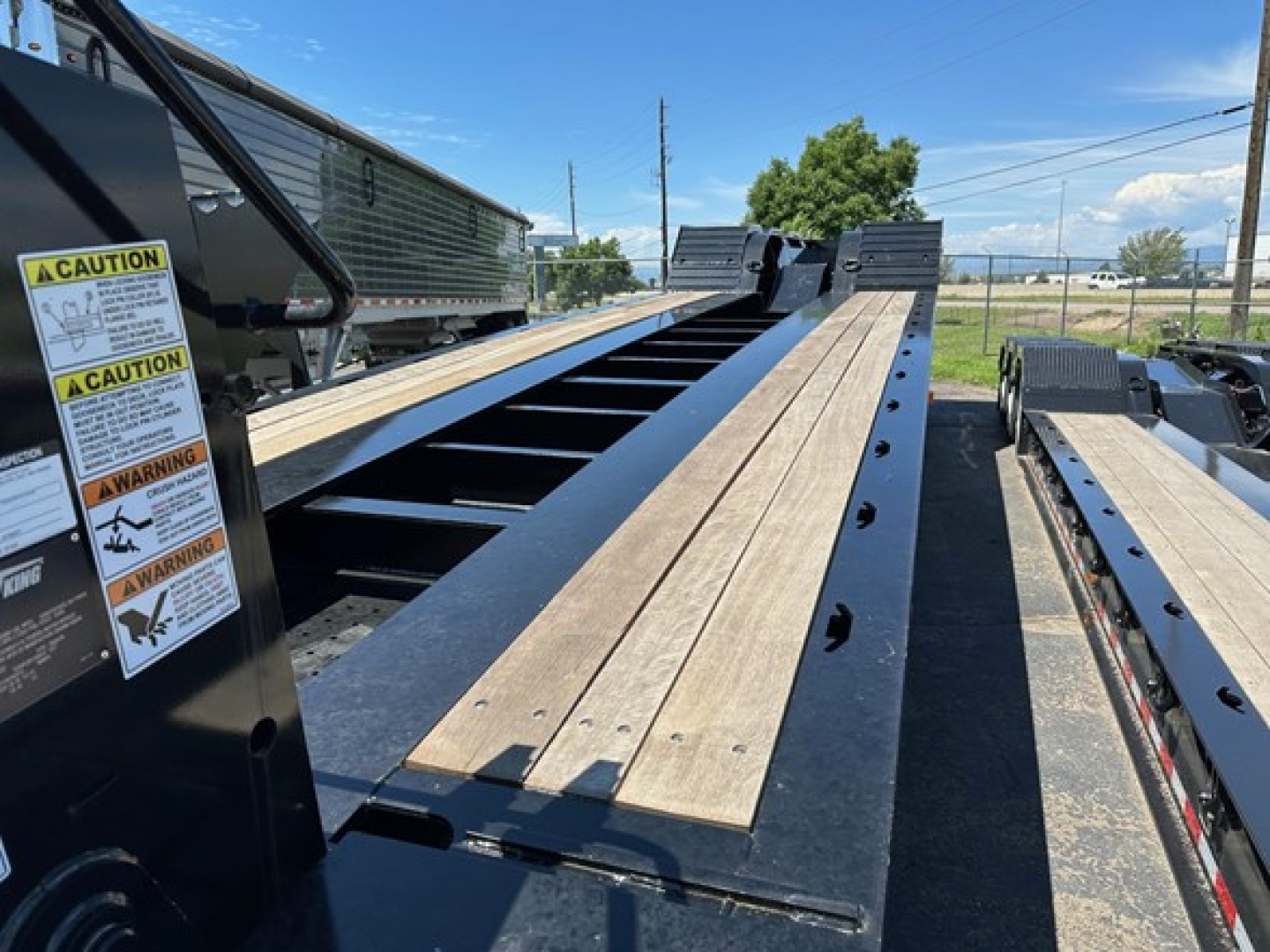 Trailer deck of a Load King 503-554-SS-SF lowboy showing wood planks on black steel frame and warning labels on side.