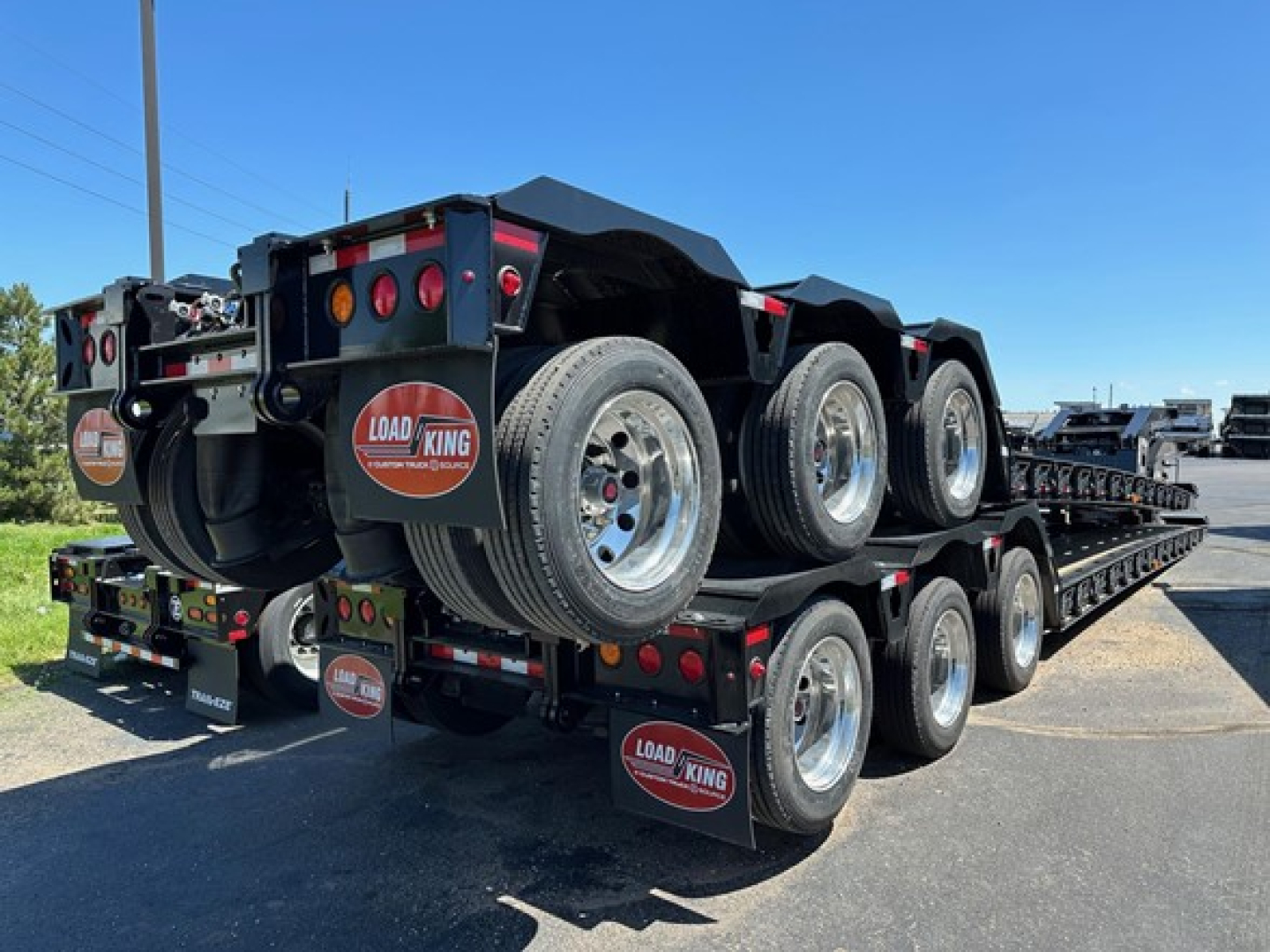 Load King trailer rear view showing triple-axle lowboy with Load King branding on mud flaps and rear plate; multiple round taillights and chrome wheels visible.