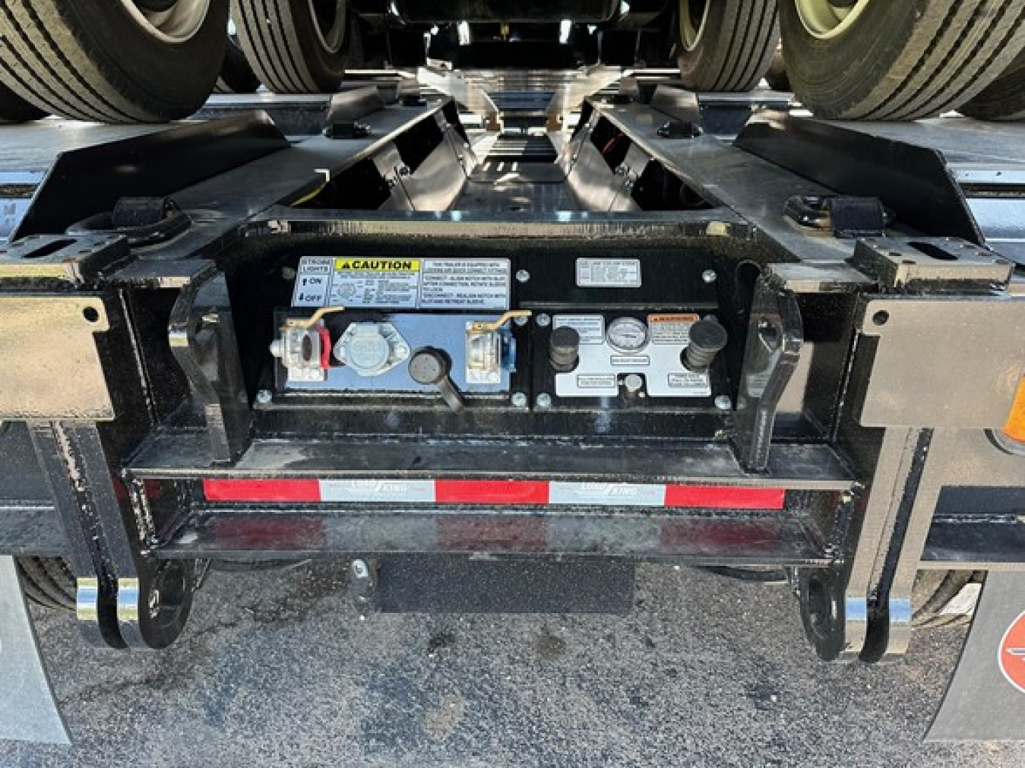 Trailer rear undercarriage showing control panel, warning label, valve connectors, and hydraulic components on a Load King lowboy trailer.