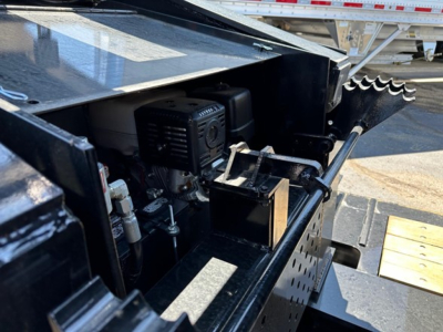 Trailer engine bay view showing diesel generator and hydraulic components on a Load King lowboy trailer, with black metal frame and control box visible.