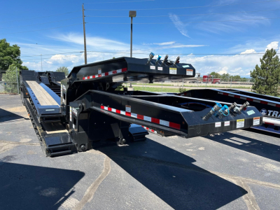 Trailer deck of a Load King lowboy trailer with extendable sections and hydraulic ramps, black with yellow safety labels and reflectors.