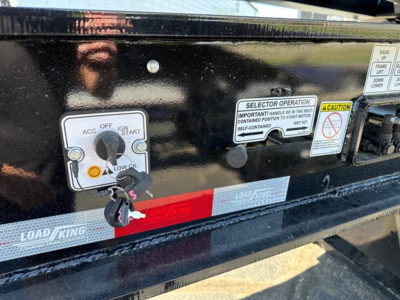 Load King trailer control panel with ACC OFF, IGN START switch, selector operation label, and caution sticker along the black frame; visible tags show LOAD KING branding.