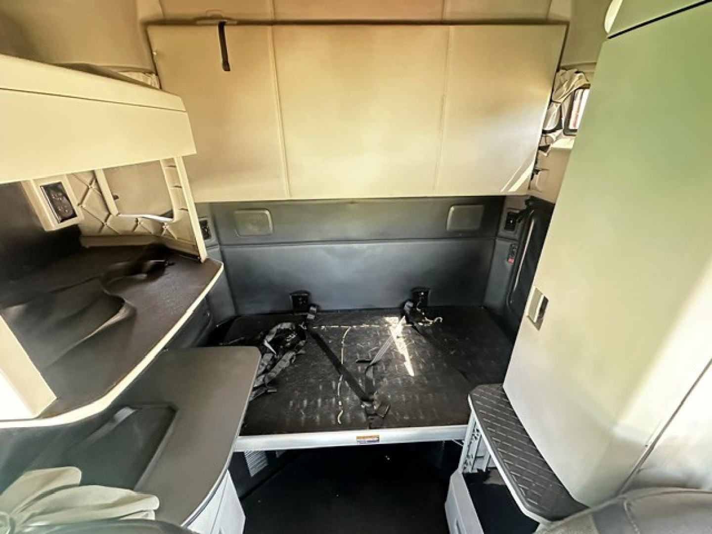 Kenworth T680 truck interior cargo area with sleeper compartment, showing storage shelves and a raised bunk platform; metal walls and a small window on the right.
