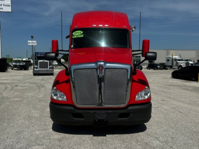 Kenworth T680 front view showing bold red cab, large chrome grille, black bumper, and side mirrors.