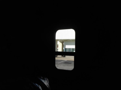 Dark cab interior with a small window showing a building and parking lot outside.