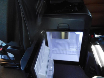 Open refrigerator/freezer in truck cab showing interior with shelves and light.