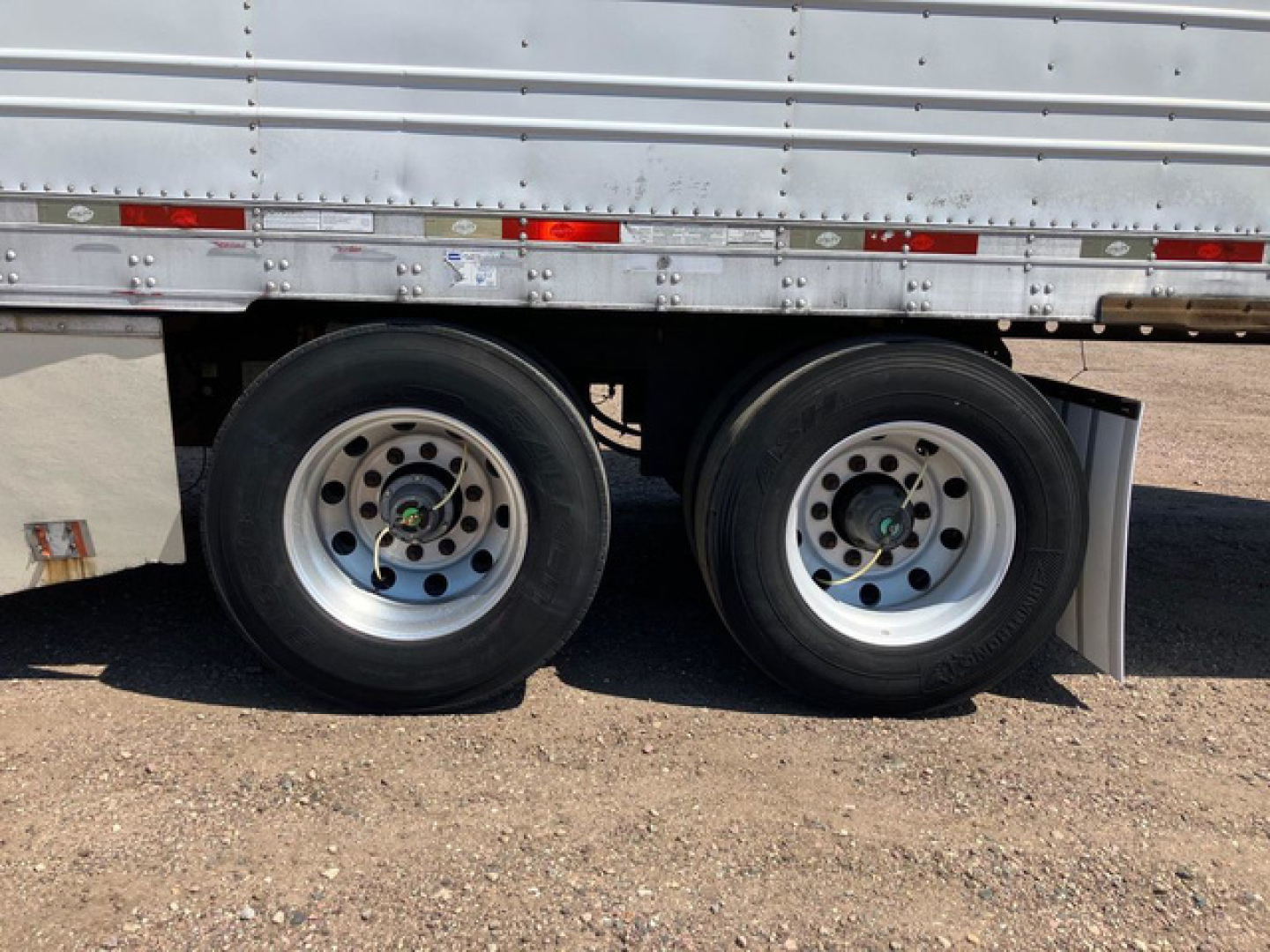 Trailer wheel area showing dual rear axles of a 2012 utility refrigerated trailer with silver side wall and reflective strips.