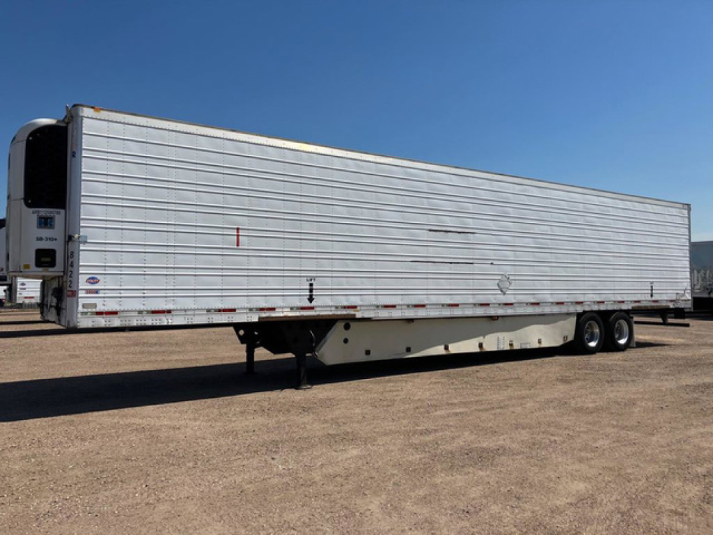Utility refrigerated trailer in side view showing aluminum ribbed exterior, tandem axles at rear, landing gear and support legs, and a nose refrigeration unit at front.