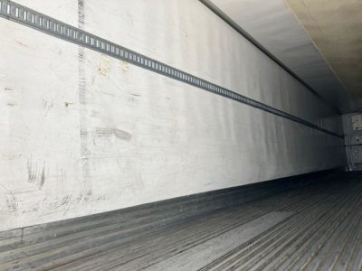 Trailer interior showing insulated metal wall with horizontal cargo track and ribbed floor surface.