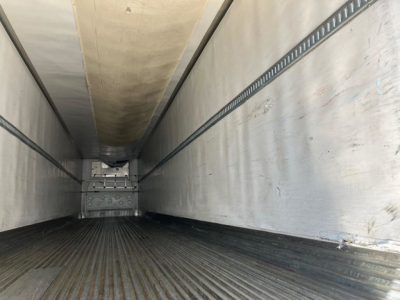 Trailer interior showing empty refrigerated trailer cargo area with ribbed floor and insulated walls, rear looking toward cab, light entering from end.