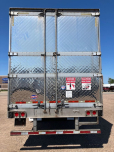 Utility reefer trailer rear showing diamond plate aluminum doors, rear bumper, taillights, and safety decals.