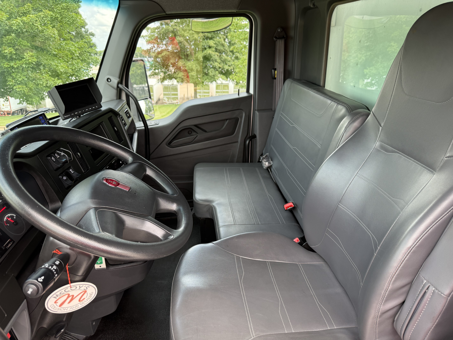 Kenworth T380 cab interior with steering wheel and two front seats; dashboard and a tablet mounted near the windshield.