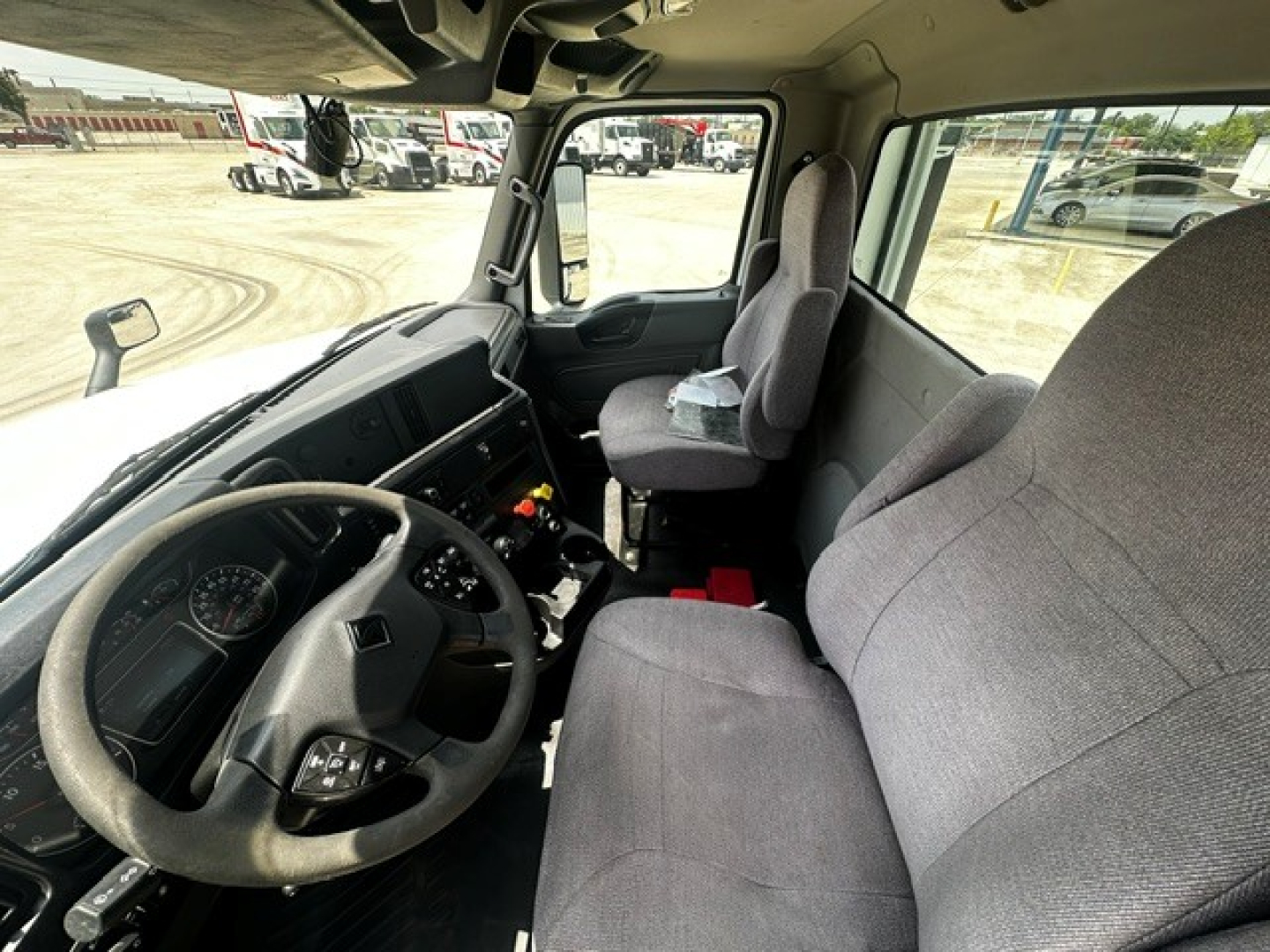 Truck cab interior showing steering wheel, dashboard, and two gray fabric seats in a cab-forward view.