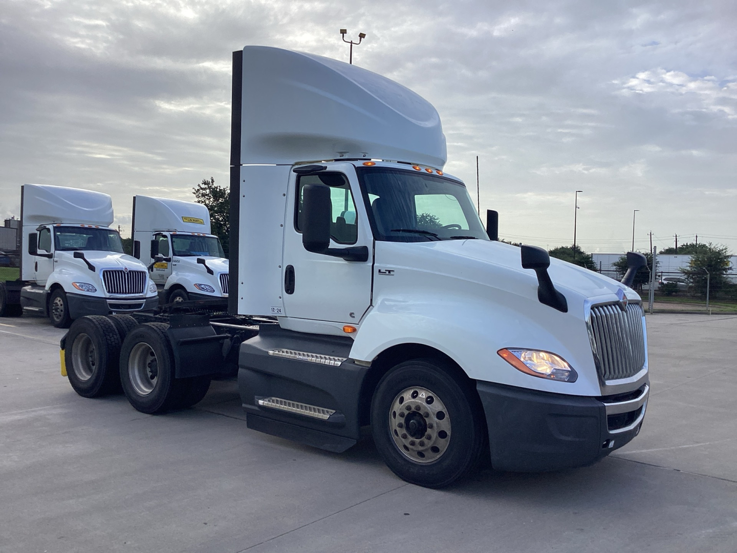 White International LT625 daycab truck in a lot with other trucks in background. Side view showing cab, fuel tanks, and dual rear axles. No visible text on the truck from this angle.