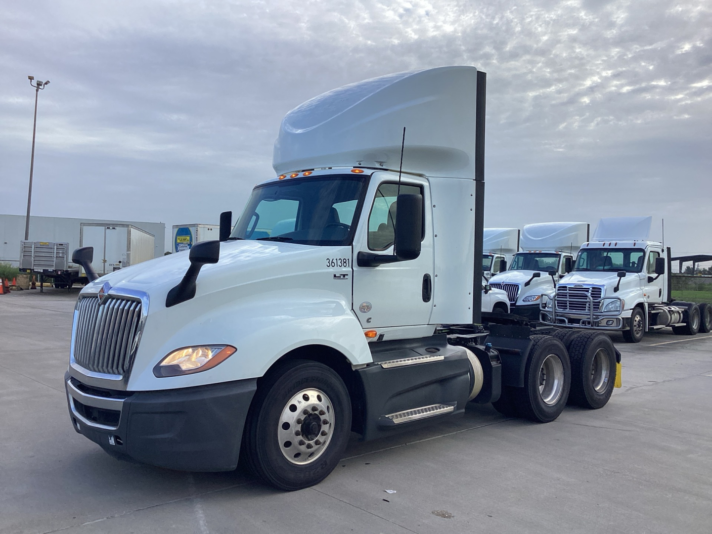 International LT625 truck in a parking lot showing a white cab and sleeper with 3-axle rear, truck front grille, headlights, and side mirrors.