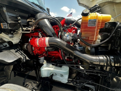 Engine bay of a 2021 International LT625 showing red engine block, black intake tubing, yellow coolant reservoir, and various hoses and components.