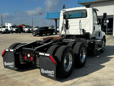 Truck chassis with cab-over tractor showing rear wheel setup and mud flaps, International LT625 logo not visible, white cab, farm/industry lot in background.