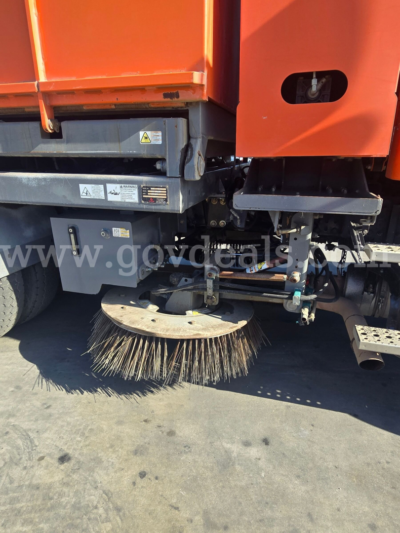 Sweeper attachment on a Freightliner M2 112 side view showing circular street sweeping brush and hydraulic supports.