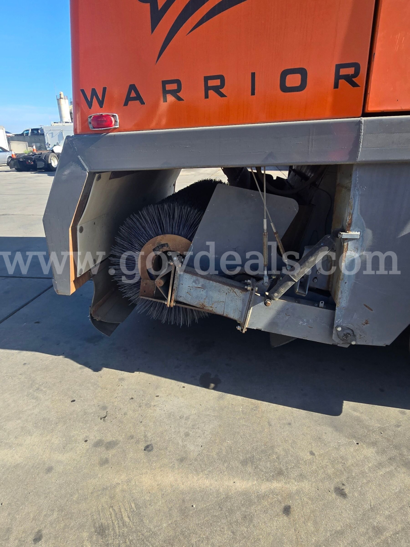 Front half of a Freightliner M2 112 sweeper showing rotating brush and side frame.