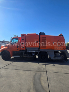 Side view of a bright orange 2015 Freightliner M2 112 sweeper truck with large rear equipment compartment and side bays.