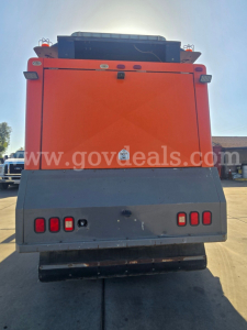 Rear view of a 2015 Freightliner M2 112 sweeper truck, orange body with gray rear bumper and black exhaust area.