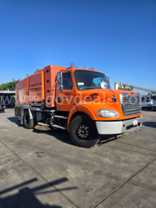 Orange Freightliner M2 112 sweeper truck in a parking lot, front-left view showing cab and large rear-compartment body.