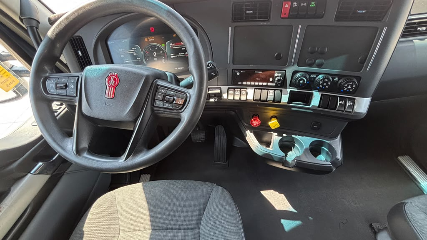 Truck cabin of a 2023 Kenworth T680 with steering wheel, dashboard controls, and center console visible.