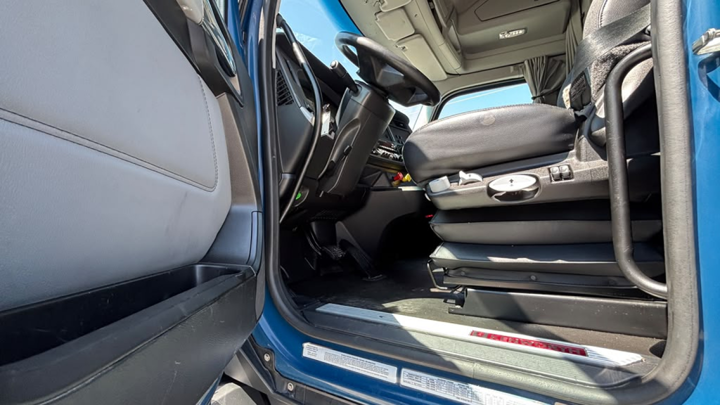 Kenworth T680 cab interior door open showing driver seat controls and dashboard.