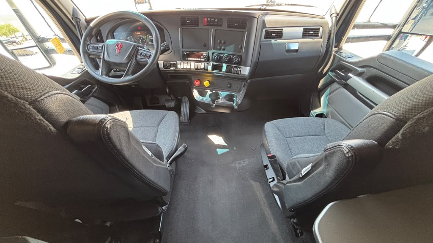 Kenworth T680 interior cabin view from driver and passenger seats; dashboard with steering wheel, control panels, gear shifter, and central console.