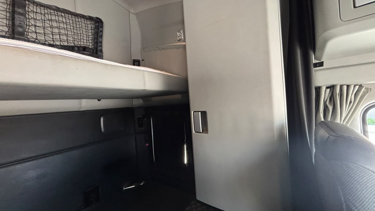 Kenworth T680 interior sleeper cab with storage shelf and partition wall, showing side bed and cabinet area.