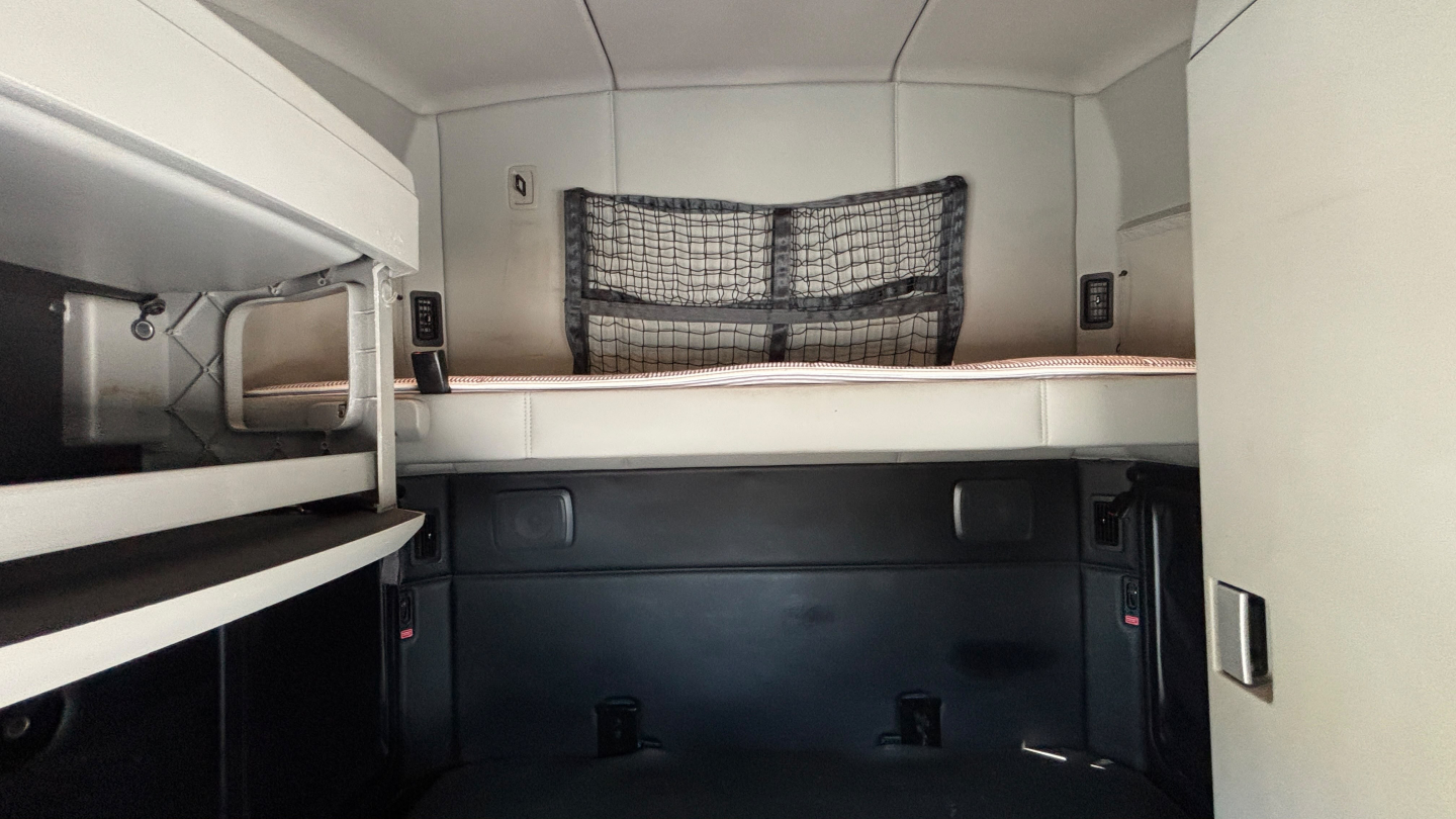 Kenworth T680 sleeper cab interior showing top bunk and storage net, side panels, and compact workspace.