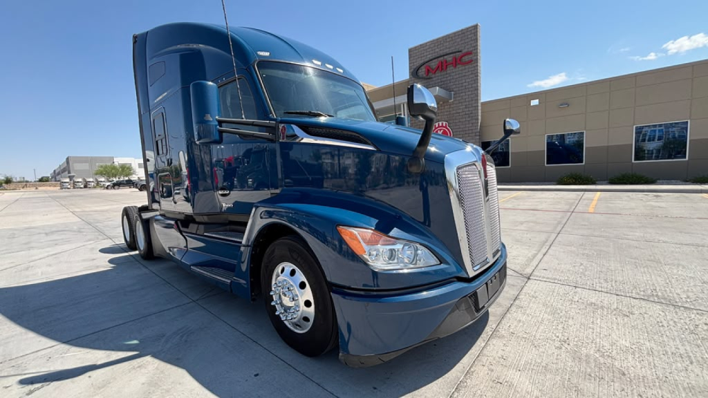 Kenworth T680 conventional sleeper truck front-left view showing blue exterior, chrome grille, headlights, and large mirrors.