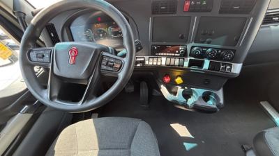 Truck cabin of a 2023 Kenworth T680 with steering wheel, dashboard controls, and center console visible.