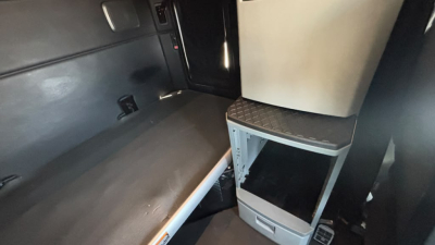 Kenworth T680 cab interior showing sleeper area and storage cabinet with open shelf and diamond plate step.