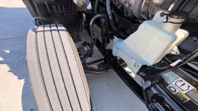 Kenworth T680 engine bay with coolant reservoir and front suspension visible in-view, showing hoses and frame components.
